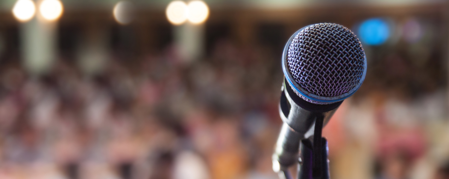 close-up of microphone with audience in background, public speaking